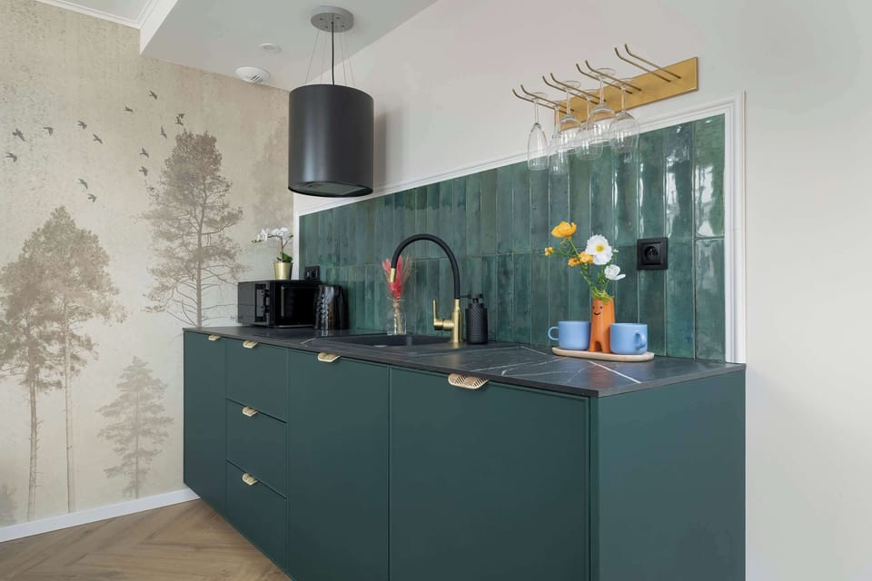 Stylish kitchenette with deep green cabinetry, patterned backsplash, and modern appliances.