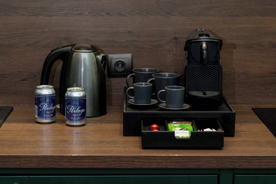 A hospitality tray with a coffee machine, kettle, cups, and complimentary supplies arranged neatly on a wooden surface.