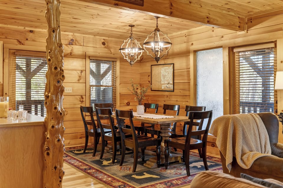 Large wooden dining table with seating for eight under decorative lighting.