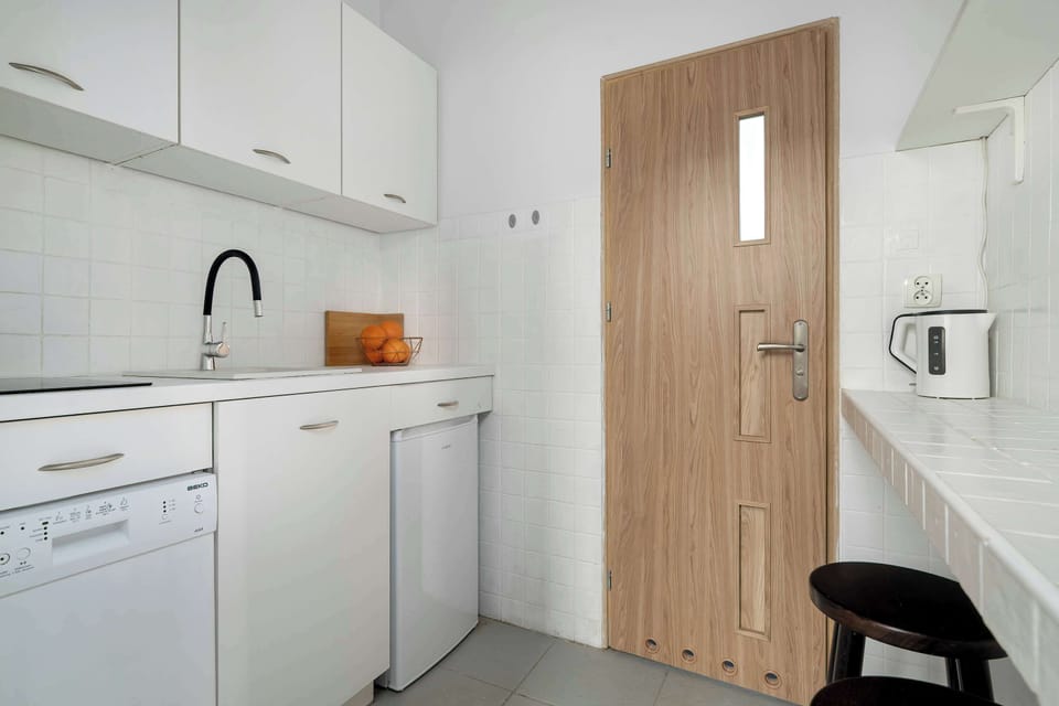 Compact kitchenette with white cabinets, sink, and wooden door in view.