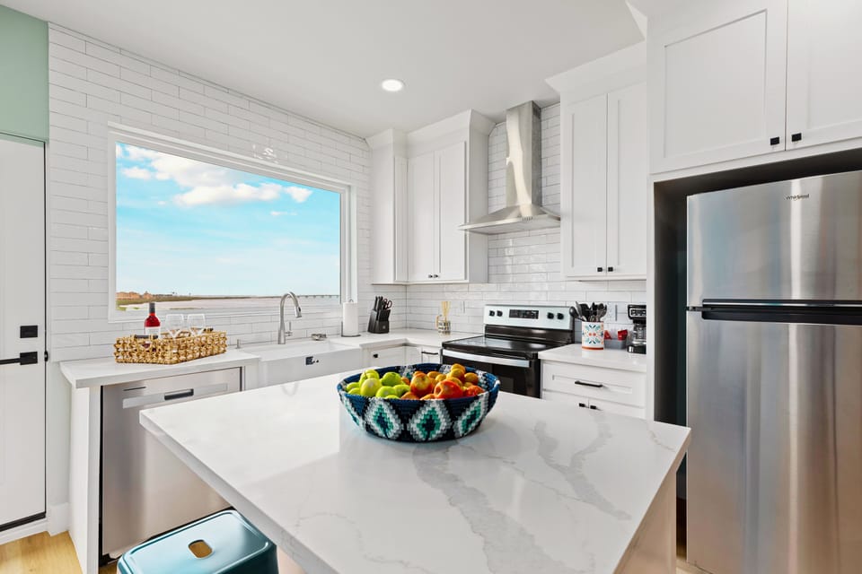 The Chef’s Kitchen: Sleek white cabinetry meets a deep farmhouse sink and stainless Whirlpool appliances. Pull up one of the three navy blue bar stools at the island and enjoy the view while you prep