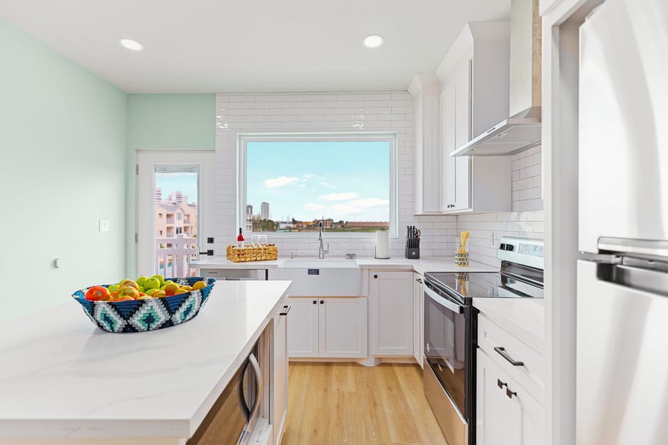 The Chef’s Kitchen: Sleek white cabinetry meets a deep farmhouse sink and stainless Whirlpool appliances. Pull up one of the three navy blue bar stools at the island and enjoy the view while you prep