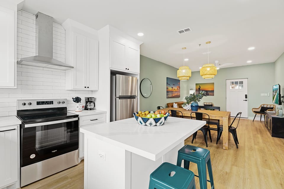 The Chef’s Kitchen: Sleek white cabinetry meets a deep farmhouse sink and stainless Whirlpool appliances. Pull up one of the three navy blue bar stools at the island and enjoy the view while you prep