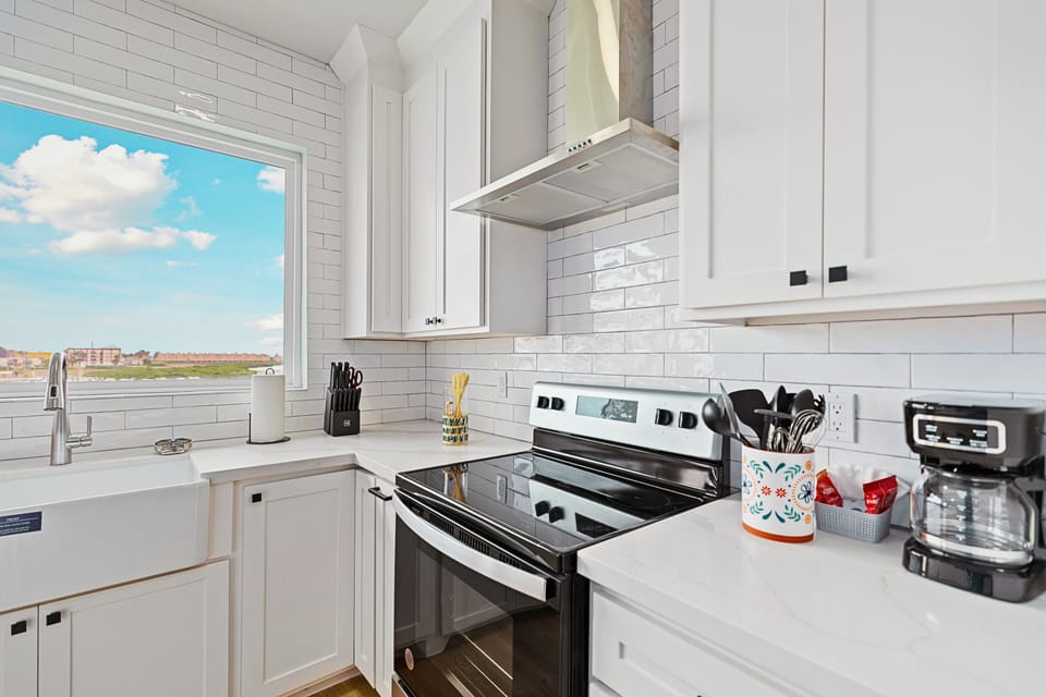 The Chef’s Kitchen: Sleek white cabinetry meets a deep farmhouse sink and stainless Whirlpool appliances. Pull up one of the three navy blue bar stools at the island and enjoy the view while you prep