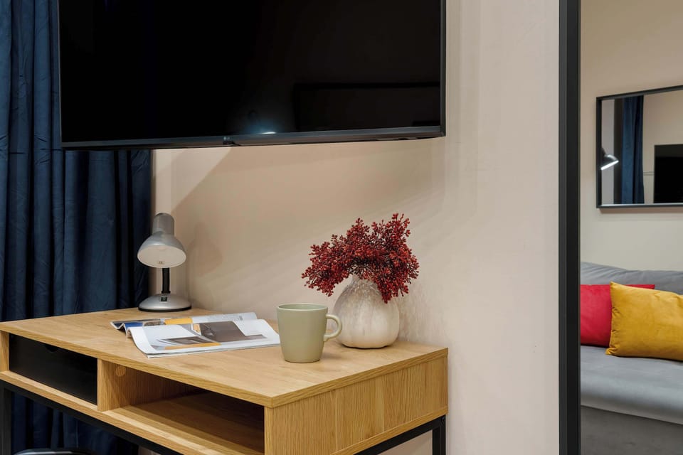 A media console with a TV and decorative accents. A lamp and plant add warmth to the scene. Dark curtains frame the window nearby.