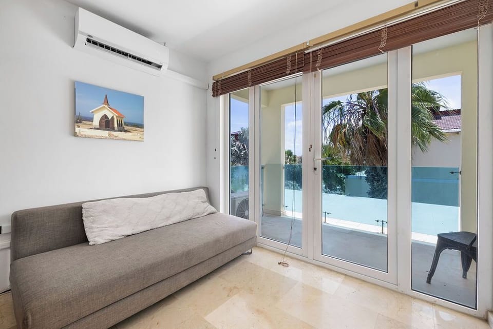 Relax in your bright living space with AC, a comfy sofa, and glass doors opening to your private terrace with tropical pool views.