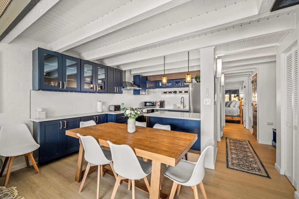 Your stylish open-plan kitchen features navy blue cabinets and a warm wooden dining table where you'll enjoy meals together.