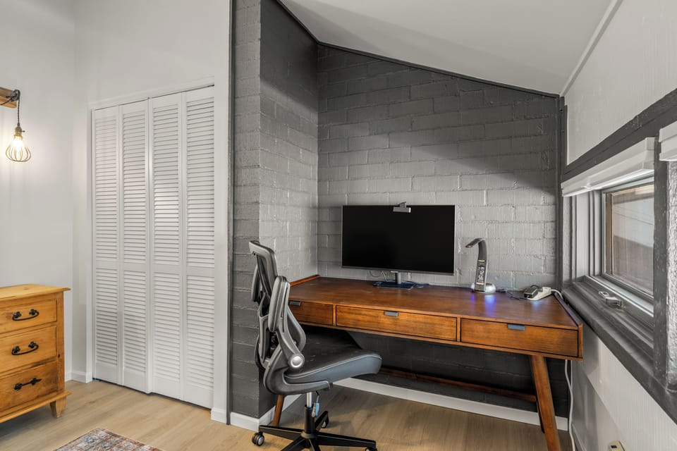 Your stylish workspace awaits with a sleek wooden desk,  and an ergonomic chair, against striking gray brick walls.