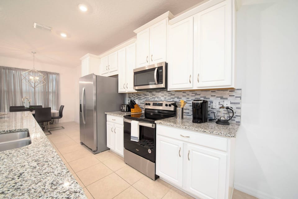 Discover culinary creativity in this sleek kitchen, featuring polished granite counters and crisp white cabinetry. Modern stainless-steel appliances and a stylish tiled backsplash enhance your cooking adventures.