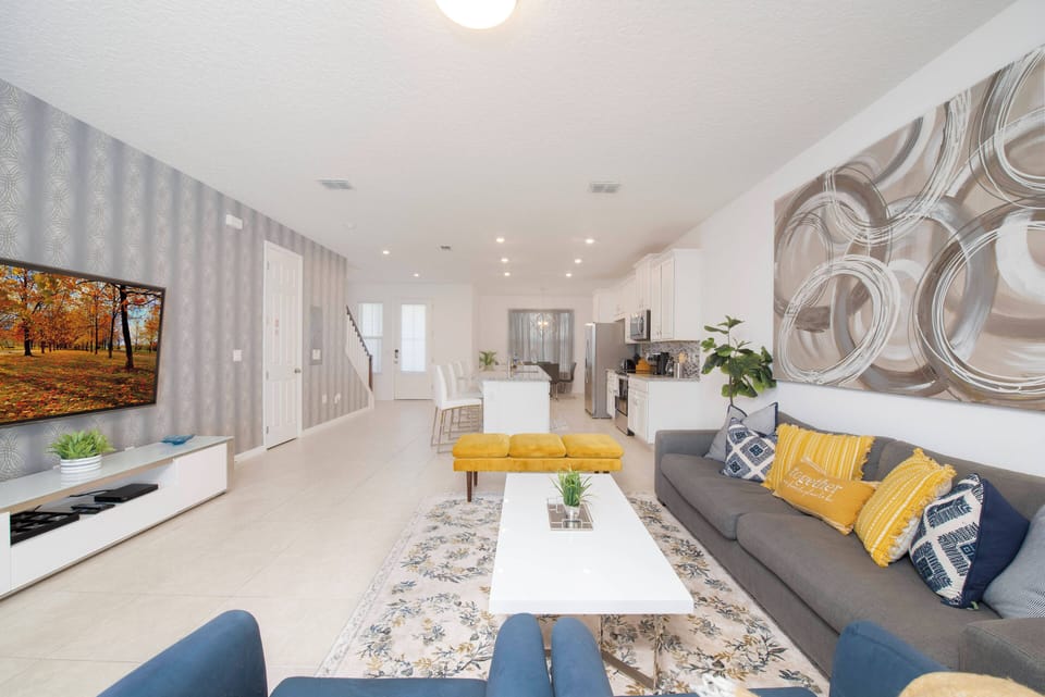 Relax in our stylish living room with a sleek gray sofa and vibrant yellow cushions. The open layout leads to a bright dining area featuring modern fixtures and a chic coffee table, creating a warm and welcoming atmosphere.