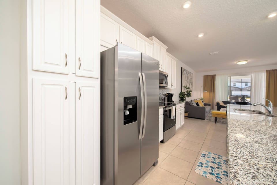 This stylish kitchen boasts sleek stainless steel appliances and bright white cabinets, creating an airy feel. Elegant granite countertops and colorful tile accents inspire culinary creativity and invite social gatherings.