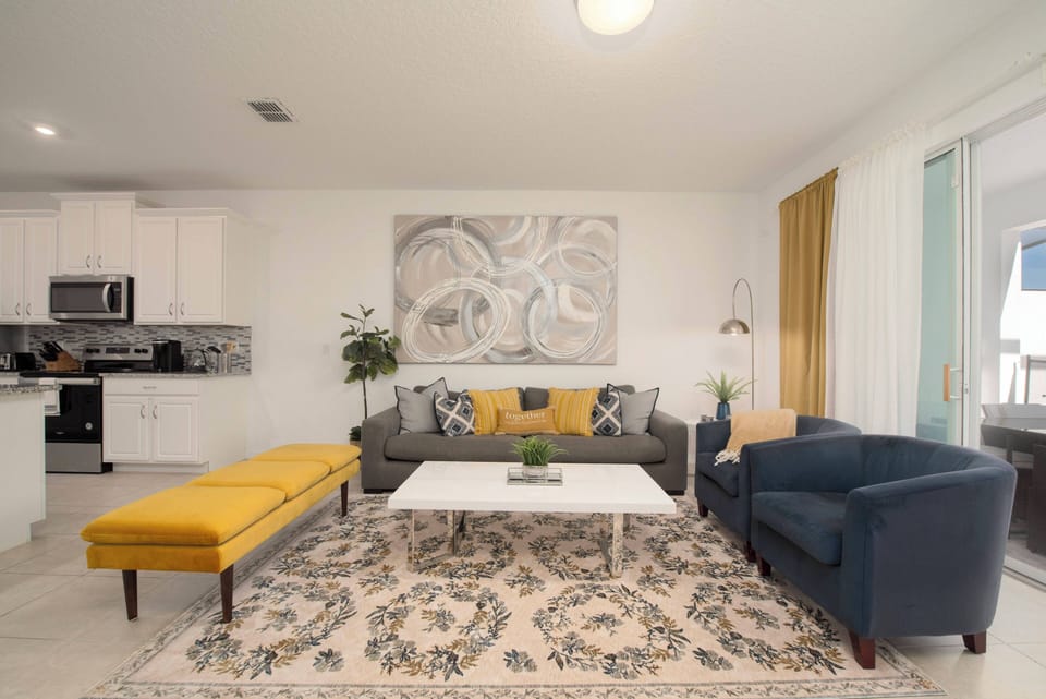 Welcome to a bright living area featuring a cozy gray sofa and a cheerful yellow bench, ideal for relaxation. The artistic wall decor and soft patterned rug enhance the modern kitchen, creating a stylish and inviting atmosphere.