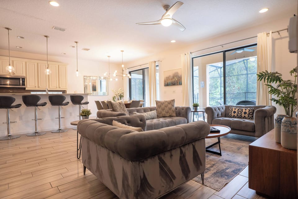 Welcome to this bright living area, where natural light pours in through large windows. The cozy sectional beckons you to relax, while the stylish coffee table and modern bar stools create a perfect blend of comfort and elegance.