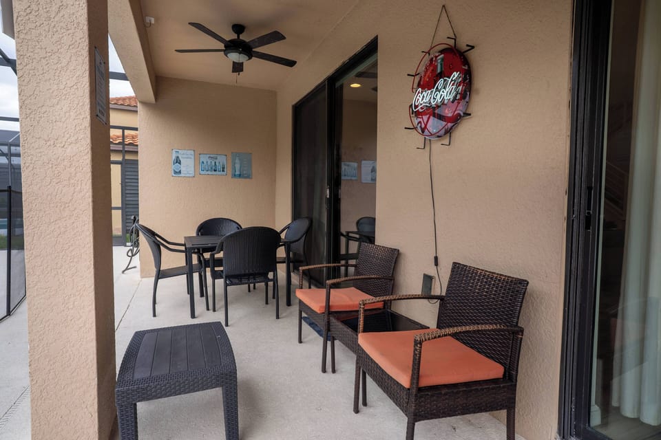 Step onto this spacious patio, where stylish wicker chairs with bright orange cushions invite you to relax. Enjoy a refreshing breeze from the ceiling fan as warm earth tones create a cozy atmosphere for your comfort.