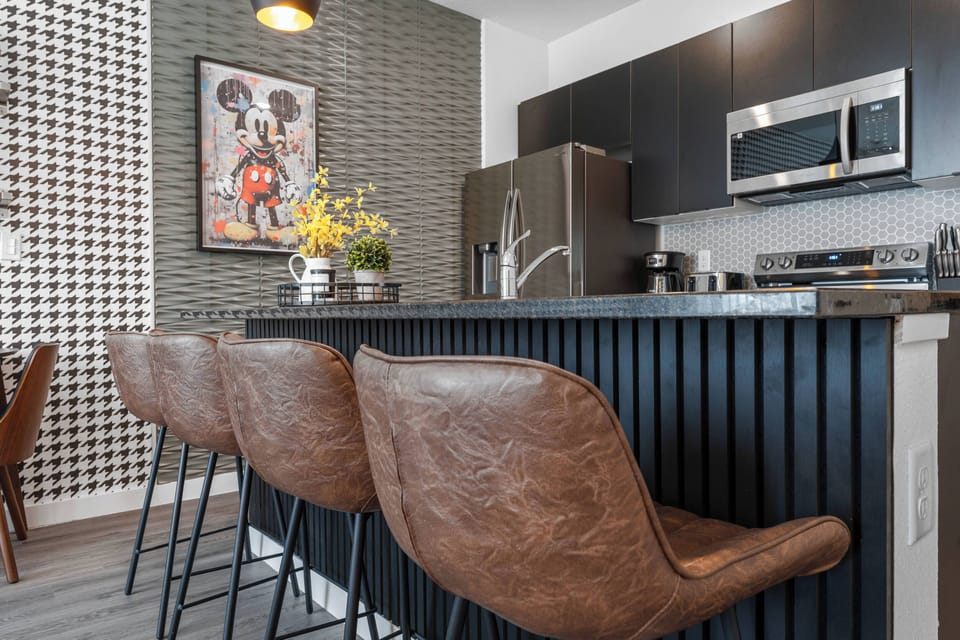 Welcome to a chic kitchen featuring rich leather bar stools and a sleek black countertop, perfect for your morning coffee. With eye-catching artwork and a vibrant patterned wall, this space is both functional and stylish.