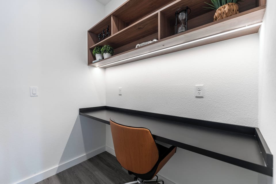 This stylish workspace features a sleek black desk and a wooden chair, ideal for guests to work or plan their next adventure, while minimalist shelves above provide decor and storage, enhancing the room's clean lines.