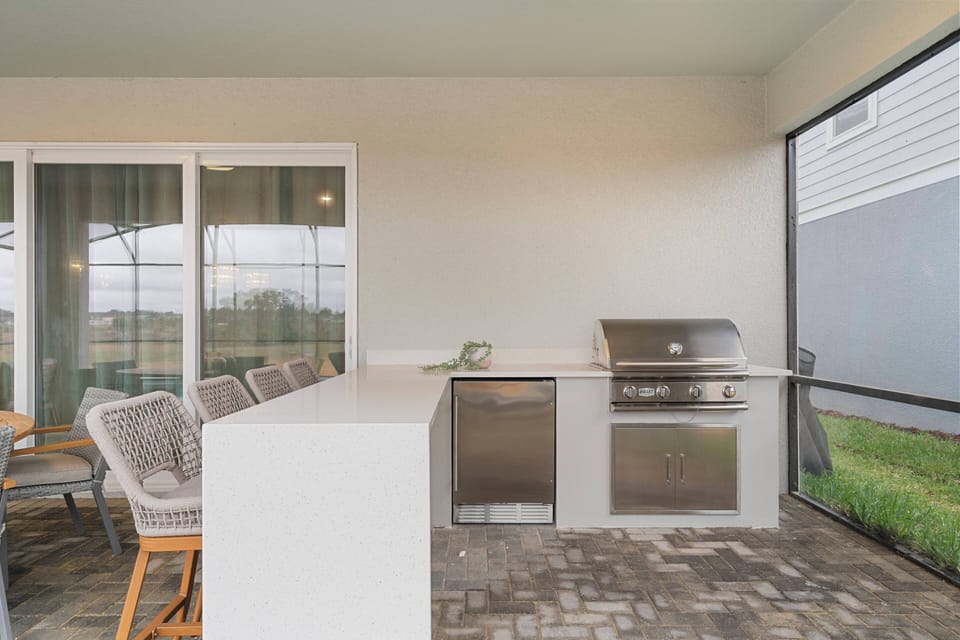 Enjoy a covered outdoor kitchen with stainless steel grill, pizza oven, sink, and sliding doors connecting to the living area, perfect for meals and relaxing outdoors.
