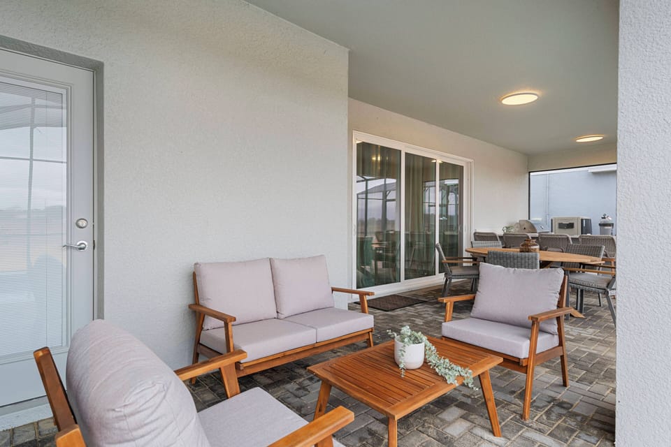 Relax on a covered patio with a round dining table, cozy outdoor seating, sliding glass doors, and peaceful green views, perfect for meals and family moments outside.
