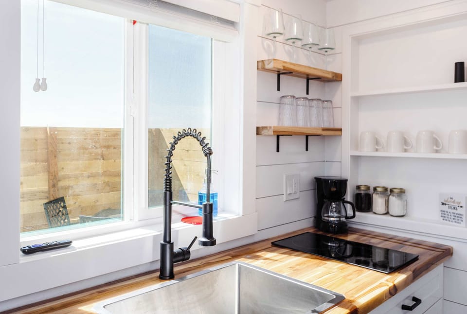 Well-equipped kitchen with cooktop, spacious sink, modern faucet, coffee maker, and open shelving for everyday meal prep.