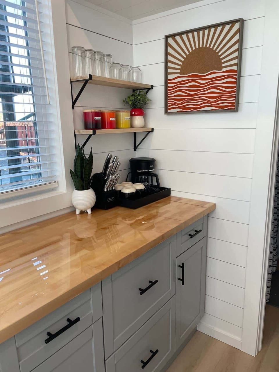 Bright modern kitchen with butcher block countertops, coffee station, open shelving, and organized storage. Thoughtfully designed tiny home kitchen perfect for cooking, coffee, and relaxing after desert adventures.