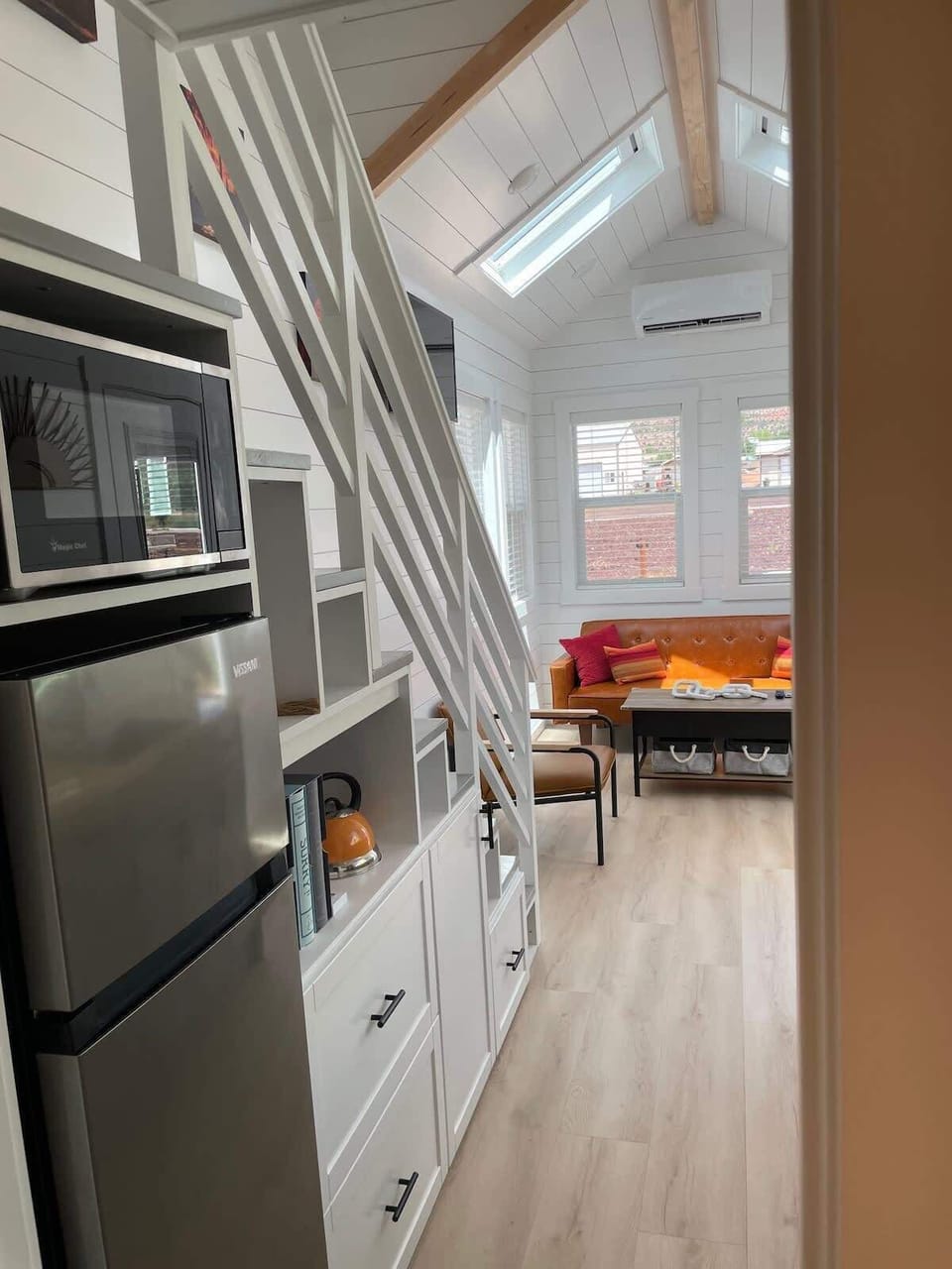 View from the kitchen toward the bright living area featuring skylights, loft access, and modern finishes throughout. Open-concept tiny home design creates a cozy and spacious atmosphere near Zion.