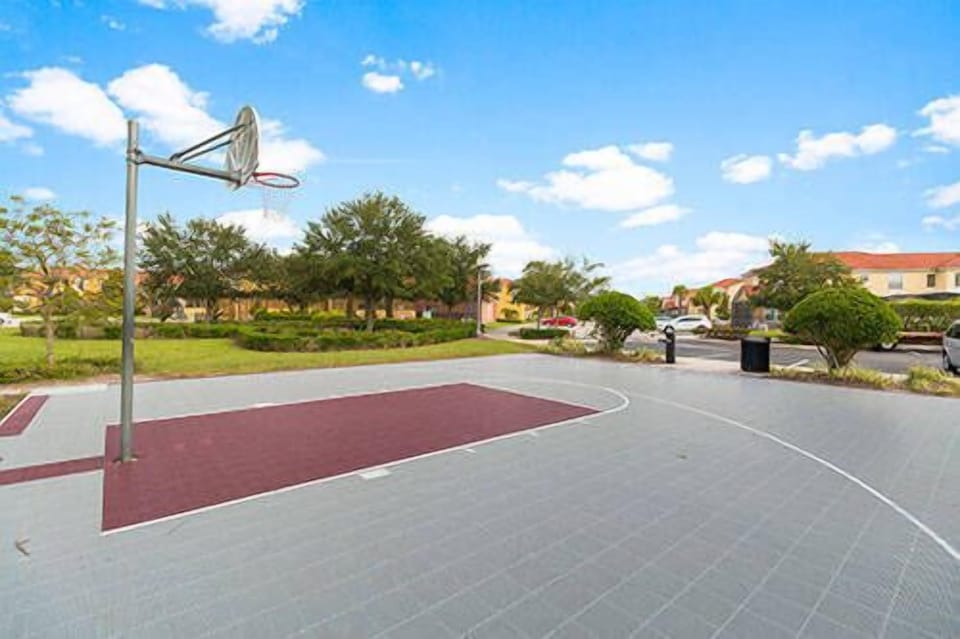 Come enjoy the basketball court with its smooth gray flooring and vibrant maroon accents, set amidst lush greenery and a bright blue sky—perfect for shooting hoops and relaxing with friends.