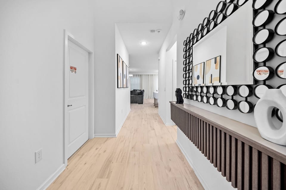 Enter a spacious hallway adorned with a captivating round mirror collection as a focal point. The warm natural wood floors harmonize with the sleek white walls, inviting you to discover the inviting open layout ahead.