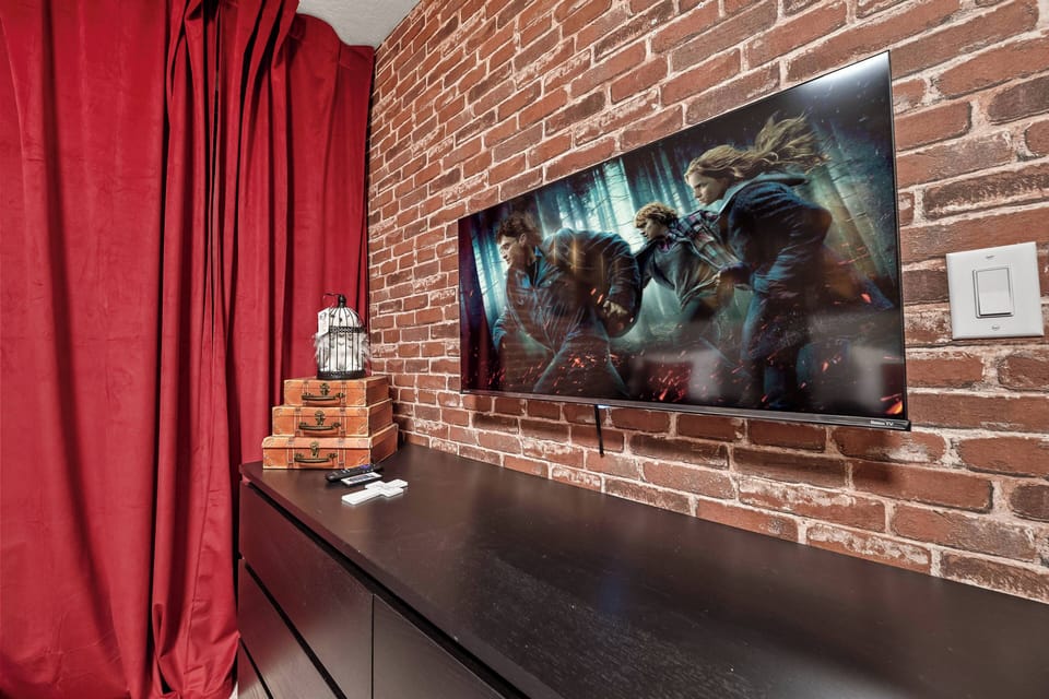 Unwind in a cozy nook with exposed brick walls and rich red curtains that set a warm atmosphere. Enjoy movie nights on the large flat-screen TV in a stylish entertainment unit, perfect for catching up on your favorite shows.