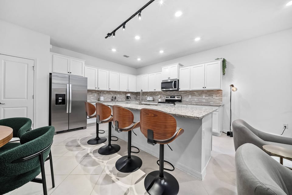 This bright kitchen boasts a stylish mix of white cabinetry and elegant marble countertops, paired with warm wood bar stools. Recessed lighting creates an inviting atmosphere, making it a perfect place for casual dining.
