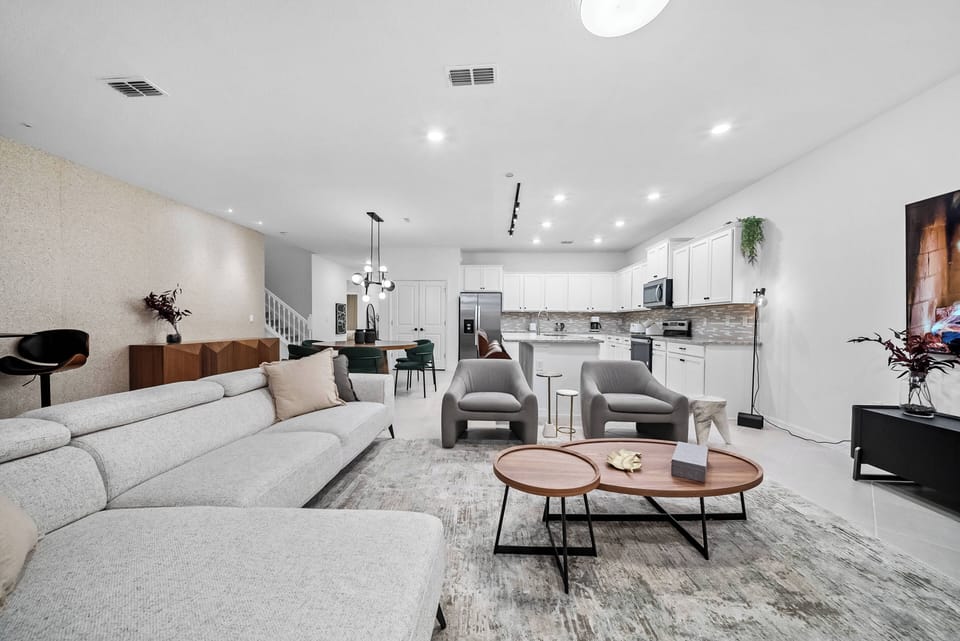 Experience comfort in this spacious living area, where a light gray sectional invites relaxation alongside sleek coffee tables. The open layout leads to a modern kitchen with stylish cabinetry, perfect for culinary adventures.