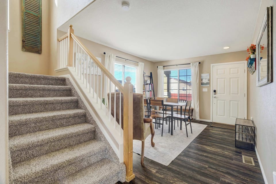 A wide, carpeted staircase with a classic wooden banister leads to the upper-level living areas and private bedrooms. Large windows nearby ensure the transition between floors is filled with plenty of natural light.
