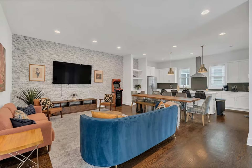 Open-concept living room with NBA Jam arcade table, plush seating, and a bright, modern kitchen.