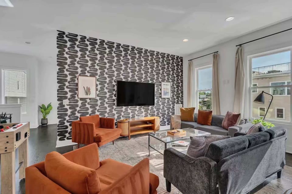 Open-concept living room with foosball table, plush seating, and a bright, modern kitchen. | Unit A