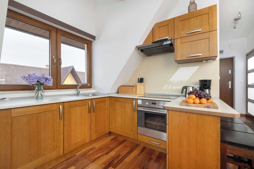 A wooden kitchen with L-shaped counters and modern appliances. The space is tidy and well-lit, suitable for everyday cooking.