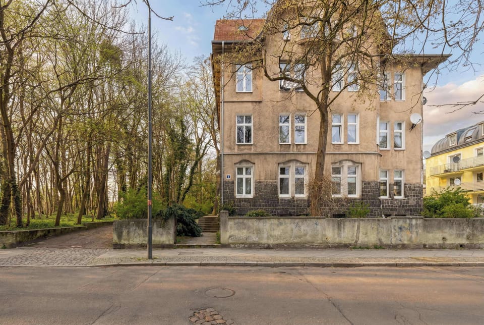 A tree-lined street in front of the building with sidewalks and parked cars. The neighborhood looks quiet and residential.