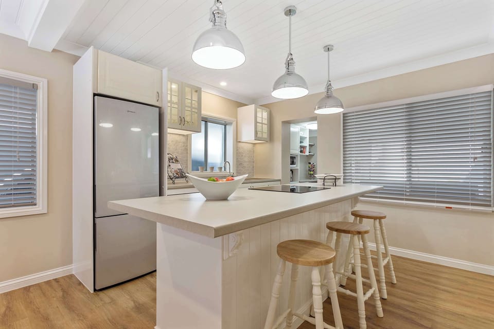 Modern kitchen with island bench, pendant lighting, stainless steel fridge, and bar stools.