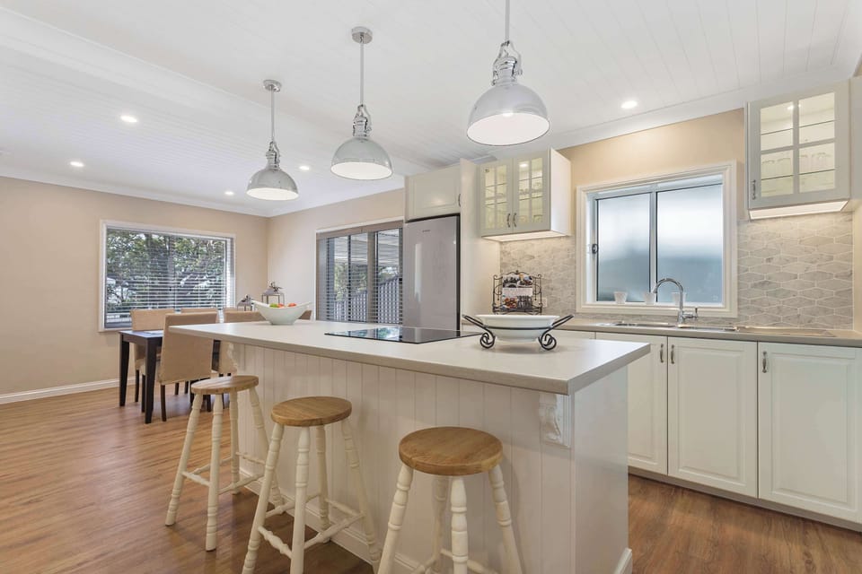 Bright kitchen with island bench, stone countertops, and wooden flooring.