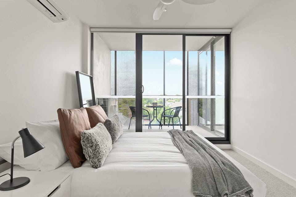 The master bedroom with a queen sized bed & a balcony with a setting.