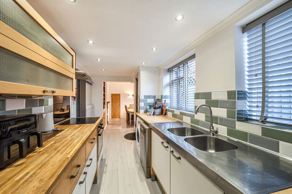 A long kitchen with wooden worktops, sink, and window blinds.