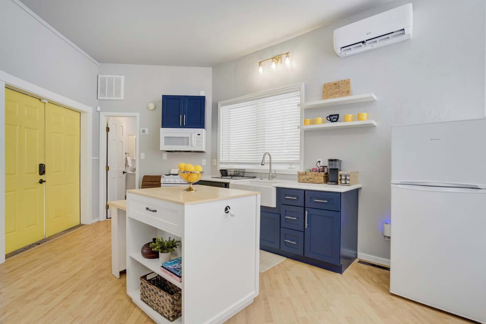 Step inside to a modern kitchenette featuring navy blue cabinetry and white open shelving that overlooks the central island, perfectly positioned for quick access to the best of downtown Colorado Springs.
