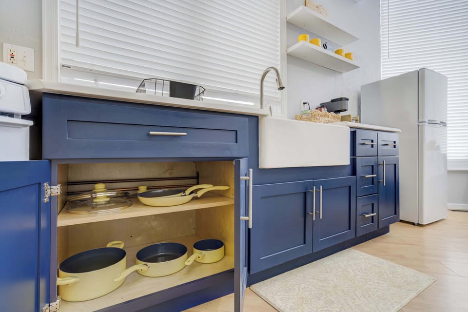 Maximize your efficiency in the modern kitchenette featuring space-saving nesting cookware and essential appliances, all tucked neatly within striking navy cabinetry positioned below your deep white farmhouse sink.