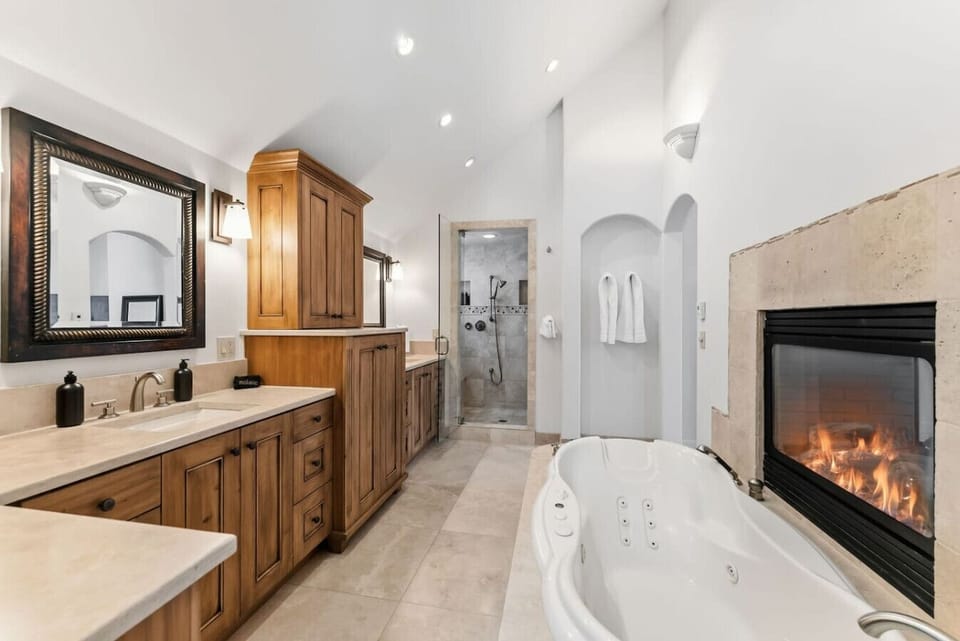 Primary bedroom with king bed, double sided fireplace, smart TV, and spa-like en suite bathroom