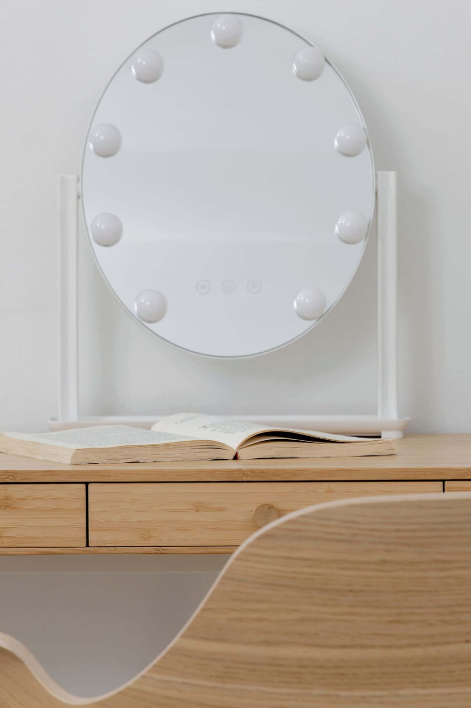 A close-up of a round mirror placed on a wooden surface. The background is neutral and clean. The detail feels modern and simple.
