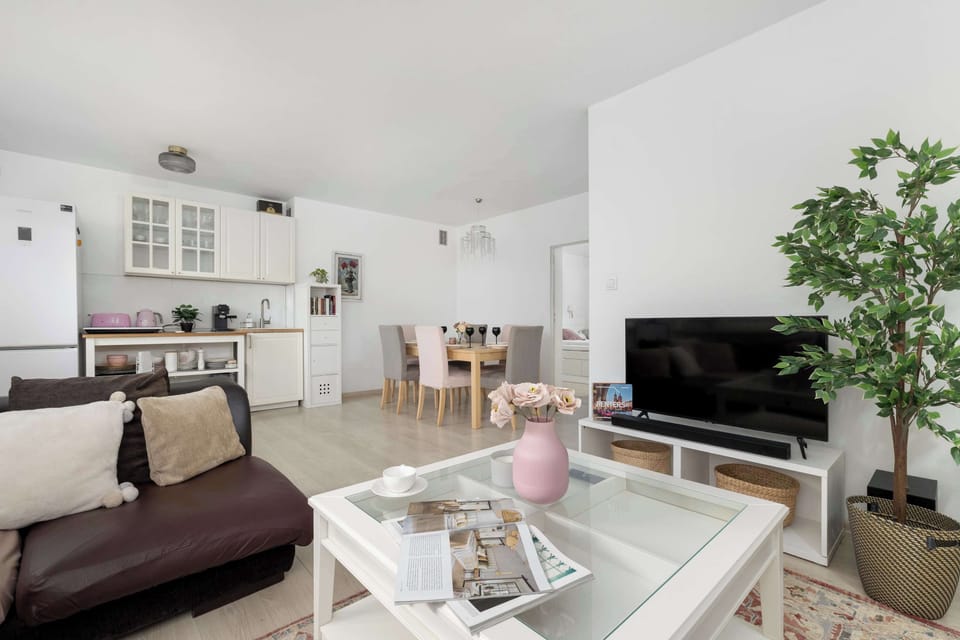 A modern living area with a glass coffee table and a dark sofa. Decorative plants and soft textiles add warmth. The room feels stylish and comfortable.