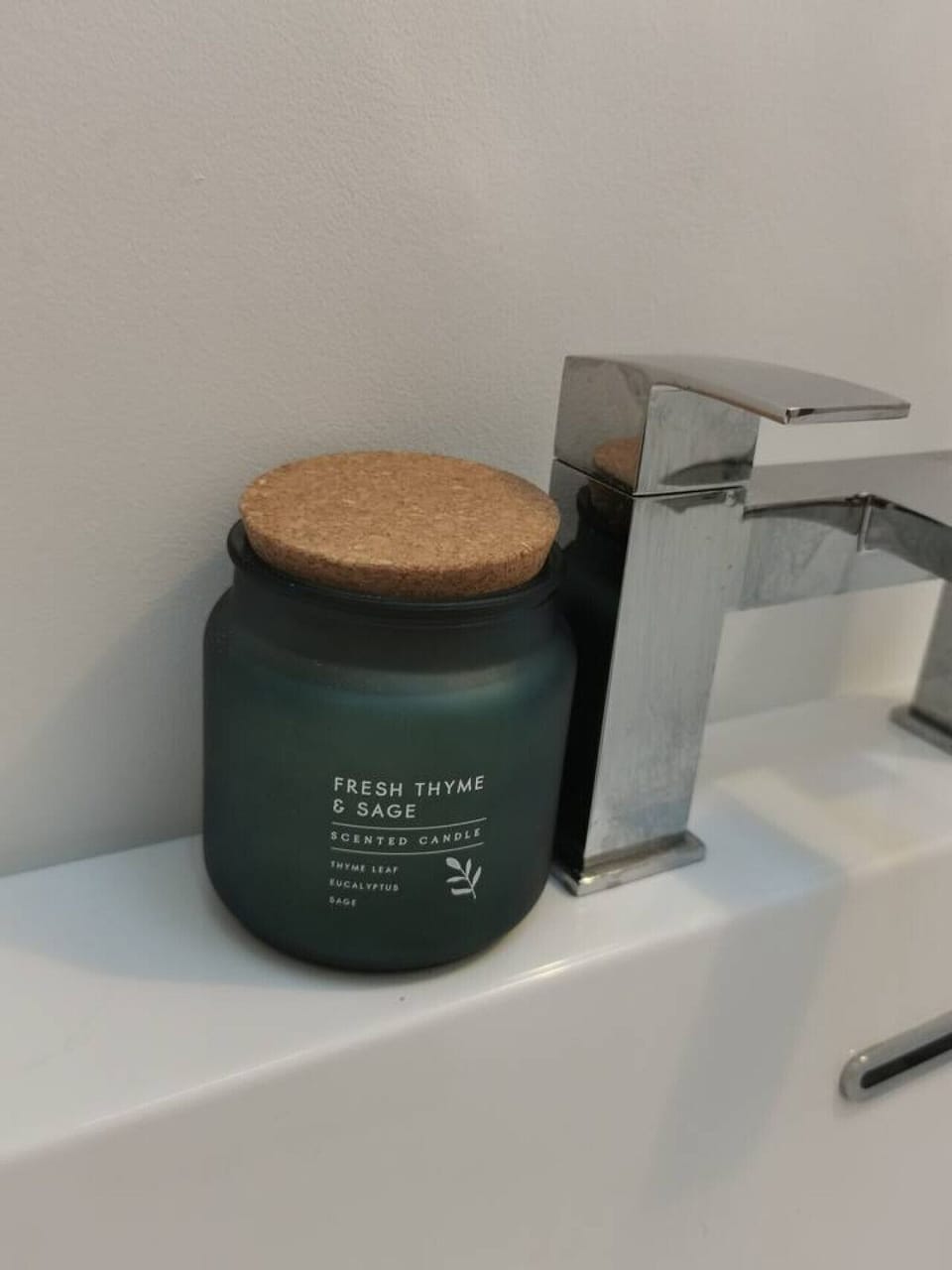 Close-up of a jar of toiletries on the edge of a sink beside a chrome tap.