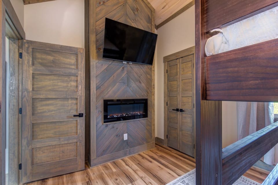 Cozy up in your rustic bedroom featuring a stunning chevron wood fireplace, flat-screen TV, and beautiful hardwood floors for ultimate relaxation.