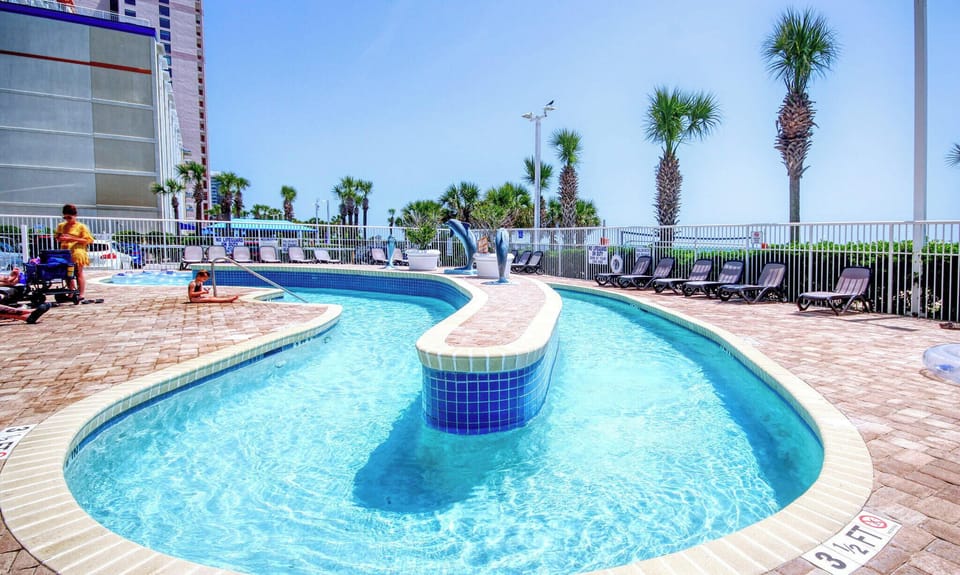 Relax in the lazy river pool with clear water, loungers, and swaying palms.