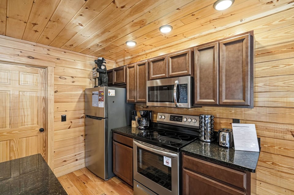 Your fully equipped kitchen features rich wood cabinets, granite counters, and modern appliances in a cozy log cabin setting.