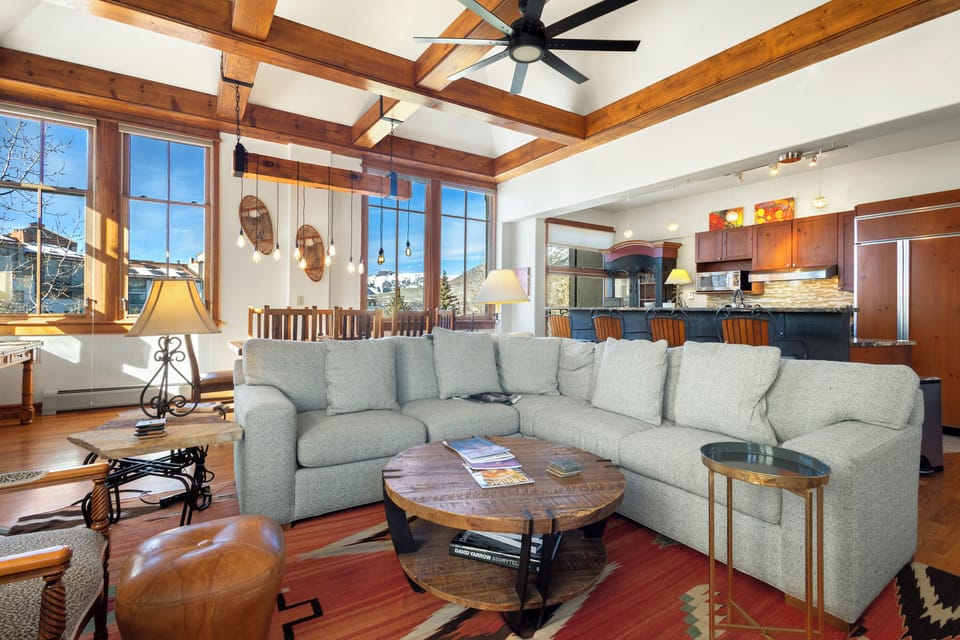 Relax in your stunning living space featuring soaring wood beams, cozy sectional seating, and mountain views through expansive windows.