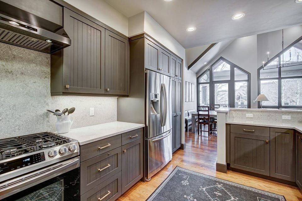 Kitchen featuring dark cabinetry, stainless steel appliances, a countertop workspace, and exterior-facing windows.